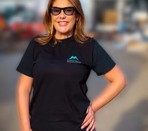 Marina Bueno em pé, de camiseta preta com a marca bordada, em área de pavilhão.