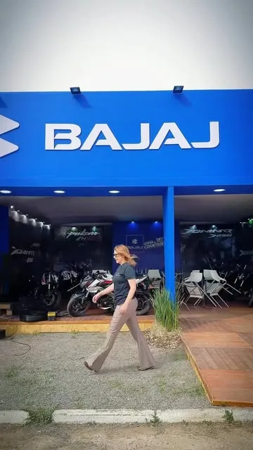 Estande Bajaj com estrutura azul, testeira iluminada e motocicletas expostas sobre deck de madeira.